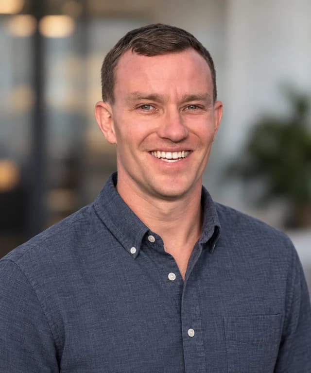 Coty Williams smiling, wearing a blue button-down shirt.